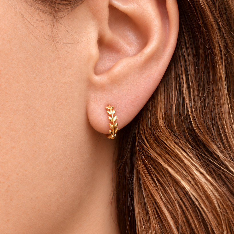 A close-up of a person's ear wearing a small gold leaf-shaped hoop earring.